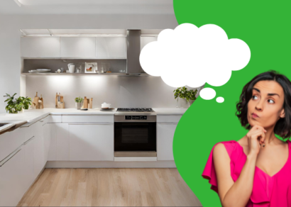 A modern, spacious kitchen with white cabinetry, stainless steel appliances, and light wooden flooring. On the right, a woman in a bright pink top appears deep in thought, with a contemplative expression and her hand on her chin. A large thought bubble emanates from her head, suggesting she is dreaming or considering ideas for home renovations, rebuilds, or remodels.