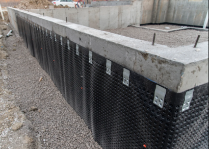 A foundation wall with waterproofing membrane installed on the exterior, showing the dimpled drainage board applied to the concrete and anchored in place