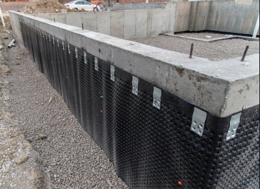 A foundation wall with waterproofing membrane installed on the exterior, showing the dimpled drainage board applied to the concrete and anchored in place